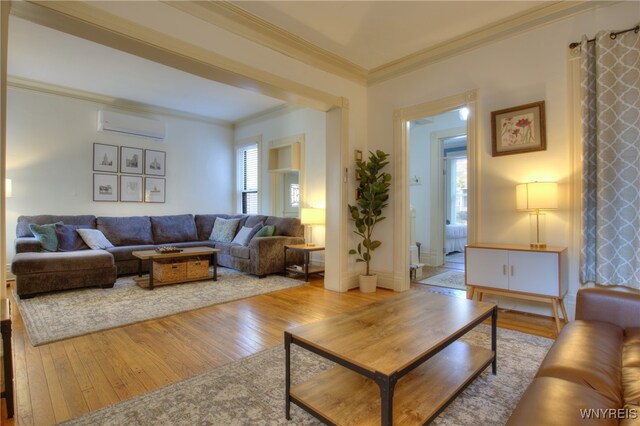 living room with a wall unit AC, light hardwood / wood-style flooring, ornamental molding, and plenty of natural light