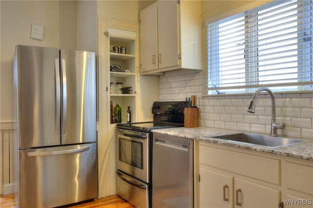 kitchen with white cabinets, backsplash, appliances with stainless steel finishes, light hardwood / wood-style floors, and sink