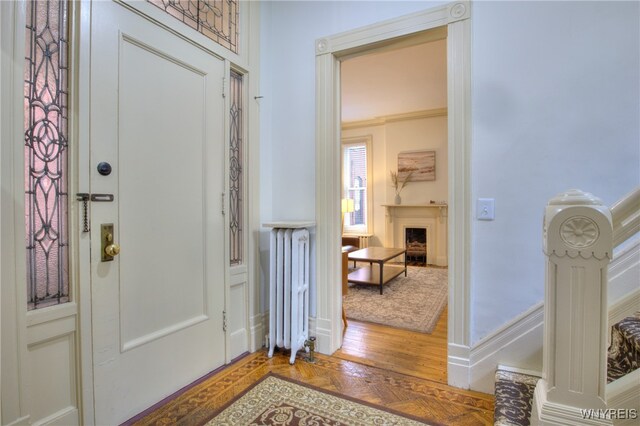 entryway featuring hardwood / wood-style flooring, ornamental molding, and radiator heating unit