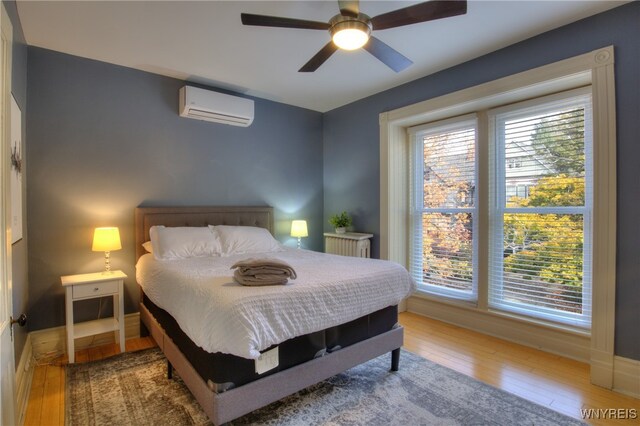 bedroom featuring hardwood / wood-style flooring, an AC wall unit, and ceiling fan