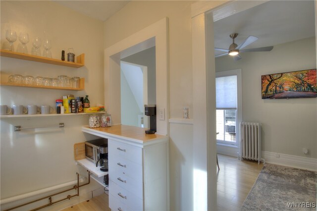 kitchen featuring white cabinets, radiator heating unit, light hardwood / wood-style floors, and ceiling fan