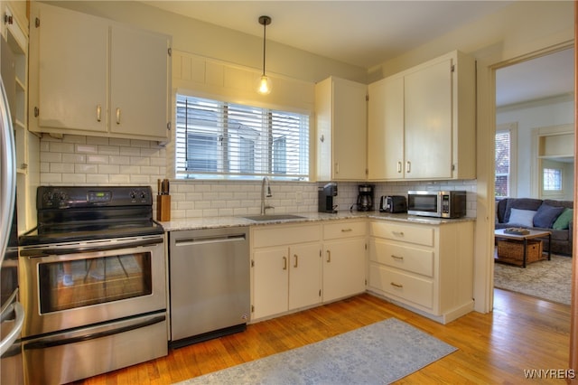 kitchen with appliances with stainless steel finishes, sink, pendant lighting, decorative backsplash, and light hardwood / wood-style flooring