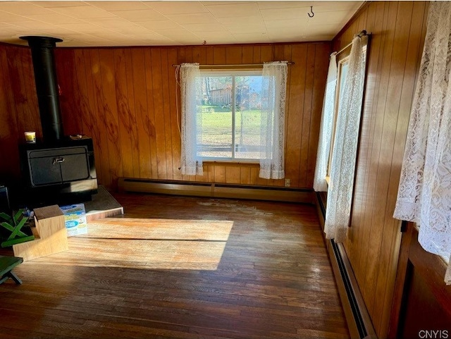 unfurnished living room featuring a baseboard heating unit, wooden walls, a wood stove, and dark hardwood / wood-style flooring