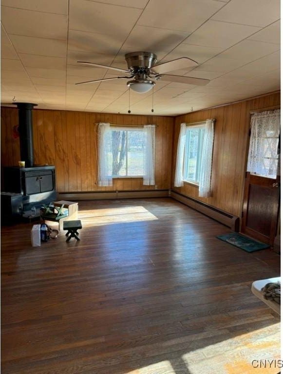 6736 Pine Grove Rd, Watson, NY 13343 - unfurnished living room featuring a wood stove, ceiling fan, a baseboard radiator, wood finished floors, and wood walls