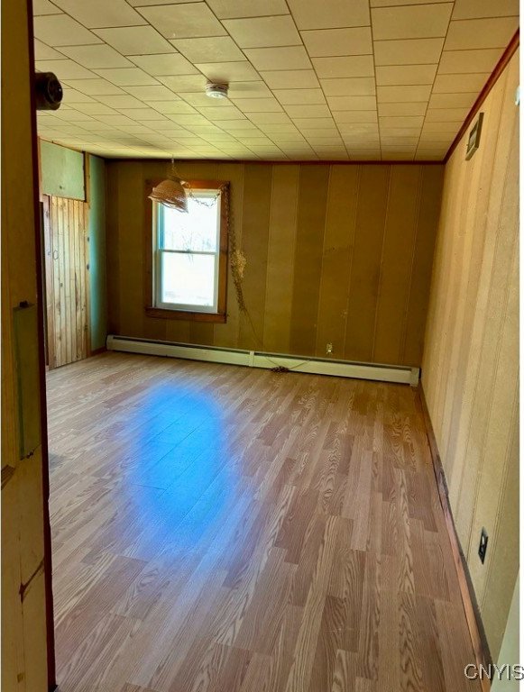 empty room featuring wood walls, a baseboard radiator, and light hardwood / wood-style flooring