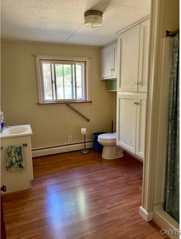 bathroom featuring hardwood / wood-style flooring, baseboard heating, toilet, and sink