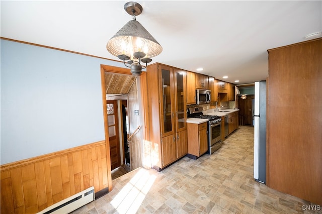 kitchen featuring baseboard heating, hanging light fixtures, sink, appliances with stainless steel finishes, and wood walls