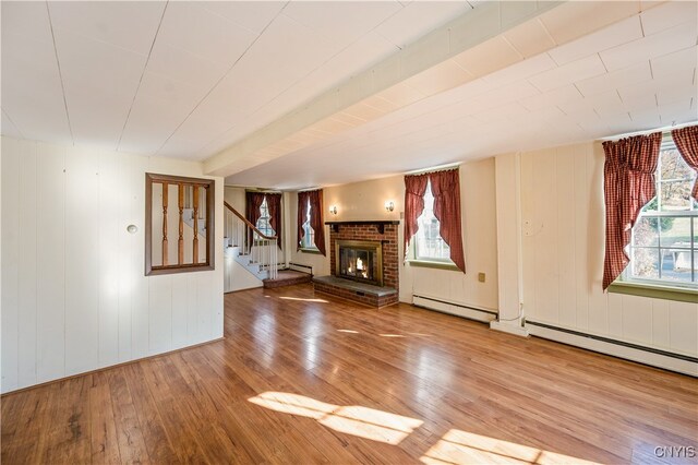 unfurnished living room featuring baseboard heating, hardwood / wood-style flooring, and a brick fireplace