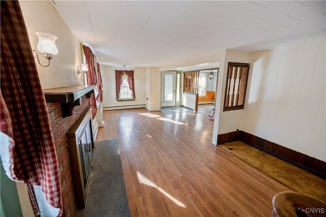 unfurnished living room featuring hardwood / wood-style floors, a baseboard heating unit, and a brick fireplace