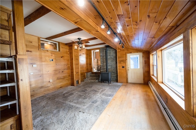 interior space with hardwood / wood-style flooring, wood walls, a wood stove, and a baseboard heating unit