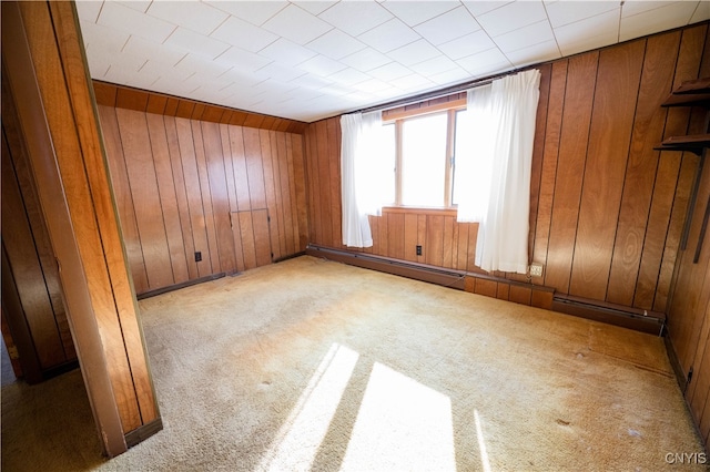 empty room with light carpet, wood walls, and a baseboard radiator