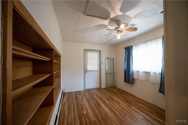 unfurnished bedroom featuring a baseboard heating unit, ceiling fan, multiple windows, and hardwood / wood-style flooring