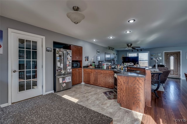 kitchen with a breakfast bar area, kitchen peninsula, light wood-type flooring, stainless steel refrigerator, and ceiling fan