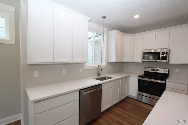 kitchen with hanging light fixtures, stainless steel appliances, sink, white cabinetry, and dark hardwood / wood-style flooring