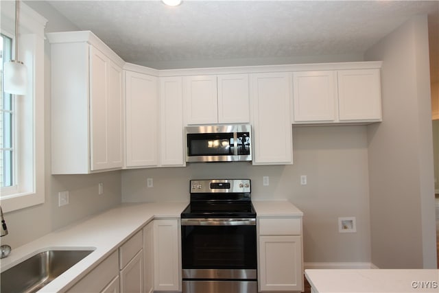 kitchen with appliances with stainless steel finishes, white cabinets, sink, and hanging light fixtures