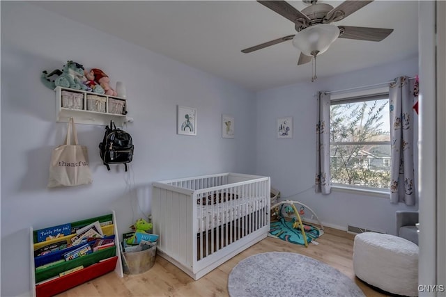 bedroom with ceiling fan, wood-type flooring, and a crib