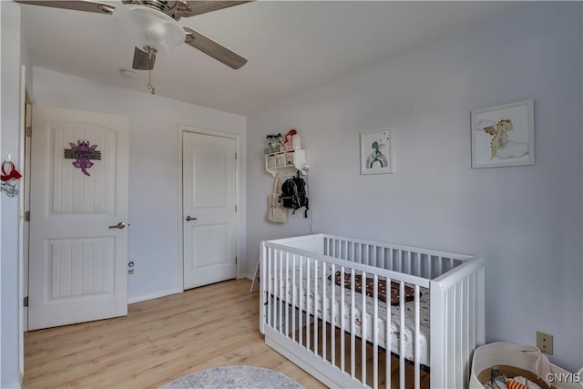 bedroom featuring a crib, light hardwood / wood-style floors, and ceiling fan