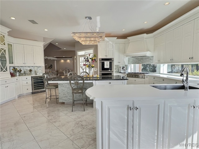 kitchen featuring sink, a kitchen island, decorative light fixtures, wine cooler, and an inviting chandelier