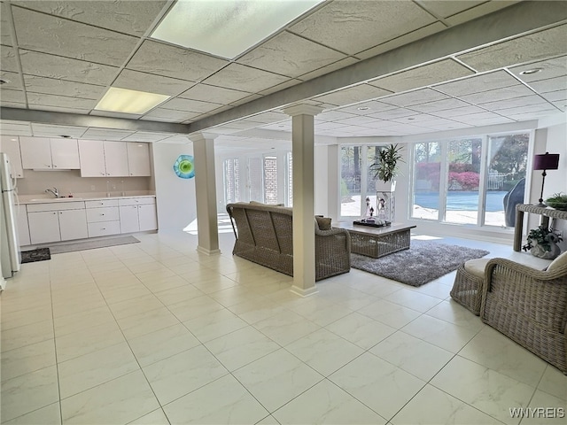 tiled living room with a drop ceiling, sink, and decorative columns