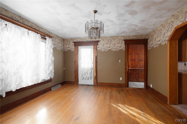 empty room featuring an inviting chandelier and light wood-type flooring