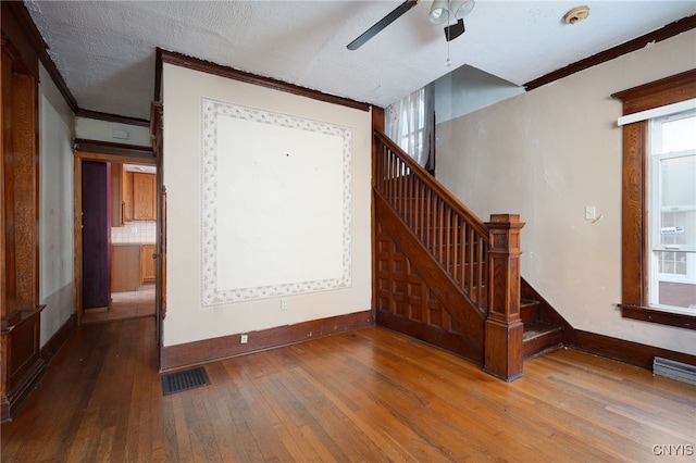 interior space with ceiling fan, a textured ceiling, ornamental molding, and hardwood / wood-style floors