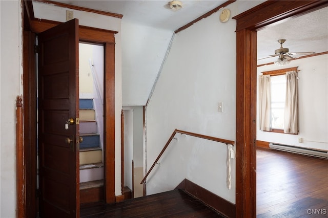 stairs with ceiling fan, wood-type flooring, a baseboard heating unit, and ornamental molding