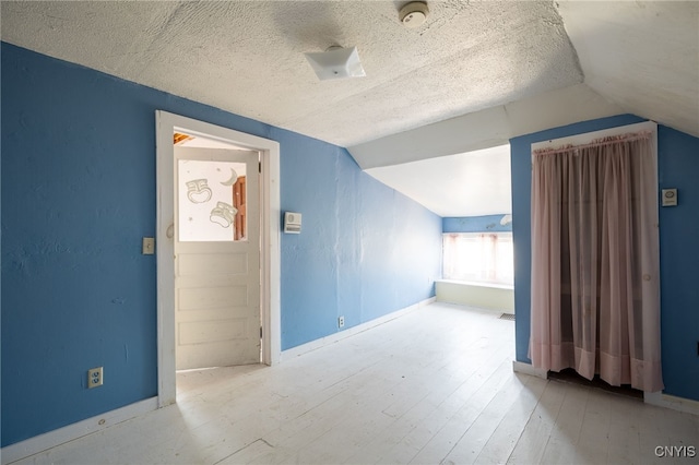 additional living space featuring light hardwood / wood-style floors, a textured ceiling, and vaulted ceiling