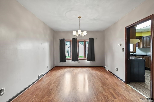 unfurnished dining area with a chandelier and light wood-type flooring