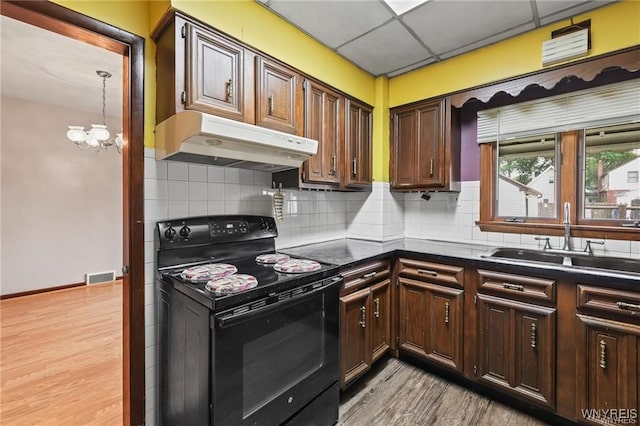 kitchen featuring decorative backsplash, black range with electric stovetop, a notable chandelier, a drop ceiling, and sink