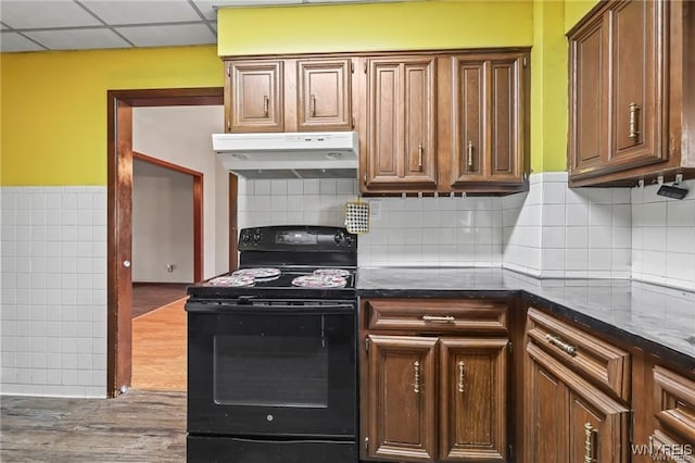 kitchen featuring black electric range, tasteful backsplash, a drop ceiling, dark stone countertops, and hardwood / wood-style flooring