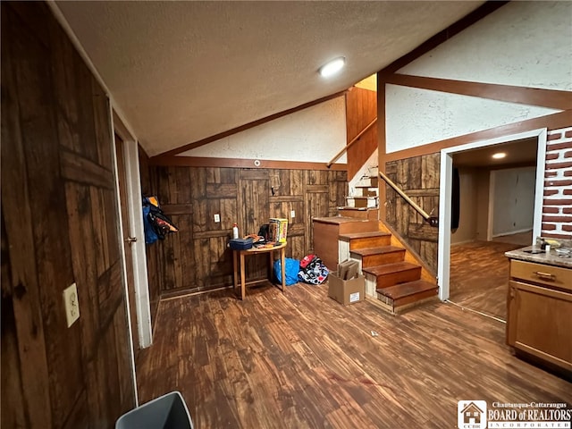 foyer featuring lofted ceiling, a textured ceiling, wooden walls, and dark wood-type flooring