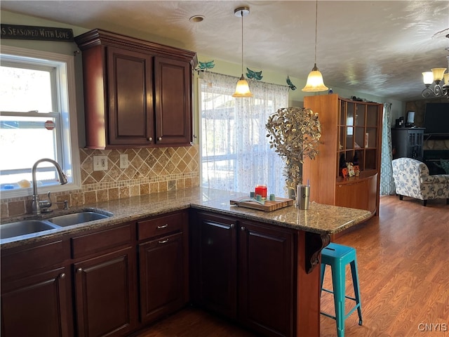 kitchen featuring kitchen peninsula, hanging light fixtures, a breakfast bar, hardwood / wood-style flooring, and sink