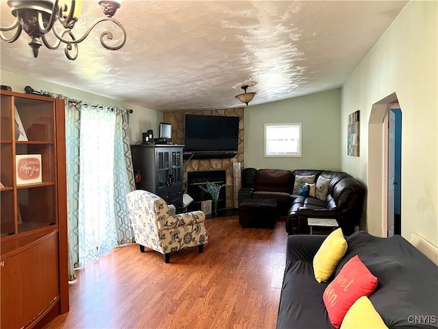 living room featuring a textured ceiling, wood-type flooring, lofted ceiling, and a stone fireplace