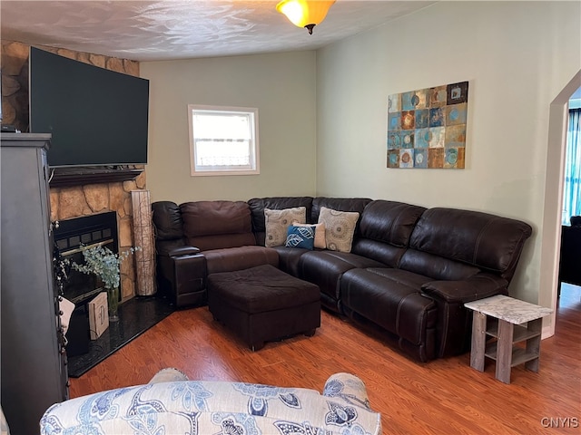 living room with a stone fireplace, lofted ceiling, a textured ceiling, and wood-type flooring