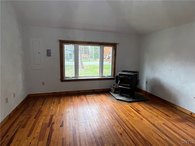 empty room with electric panel, hardwood / wood-style flooring, and a wood stove