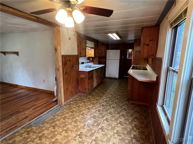 kitchen with wood walls, sink, ceiling fan, gas cooktop, and white refrigerator