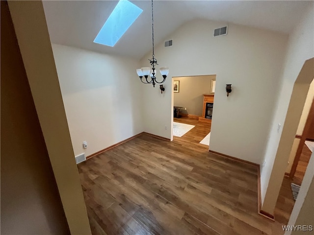 unfurnished dining area featuring an inviting chandelier, high vaulted ceiling, a skylight, and dark hardwood / wood-style flooring