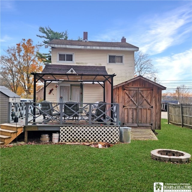 rear view of property with a pergola, a storage shed, a deck, a lawn, and a fire pit