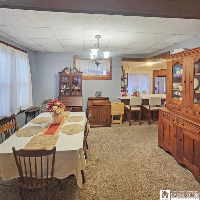 dining area with light carpet, a notable chandelier, and a paneled ceiling