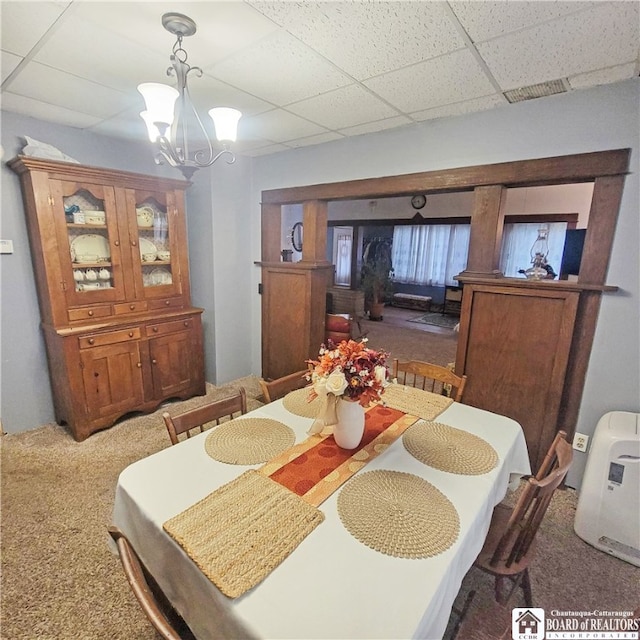 dining space featuring a drop ceiling, a notable chandelier, and carpet flooring