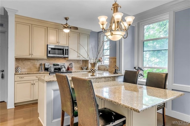 kitchen featuring cream cabinetry, stainless steel appliances, a kitchen bar, decorative light fixtures, and light stone counters