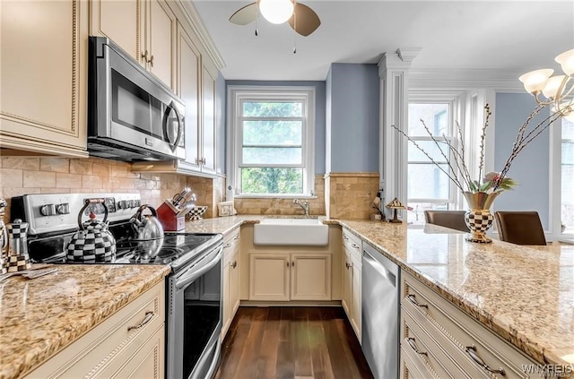 kitchen with appliances with stainless steel finishes, light stone counters, cream cabinets, and dark hardwood / wood-style flooring