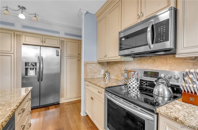 kitchen featuring light stone countertops, appliances with stainless steel finishes, cream cabinetry, and light hardwood / wood-style floors