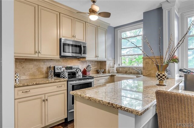 kitchen with light stone countertops, cream cabinets, sink, stainless steel appliances, and decorative backsplash