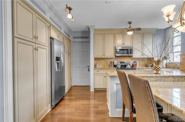 kitchen with light hardwood / wood-style floors, cream cabinets, stainless steel appliances, and light stone counters