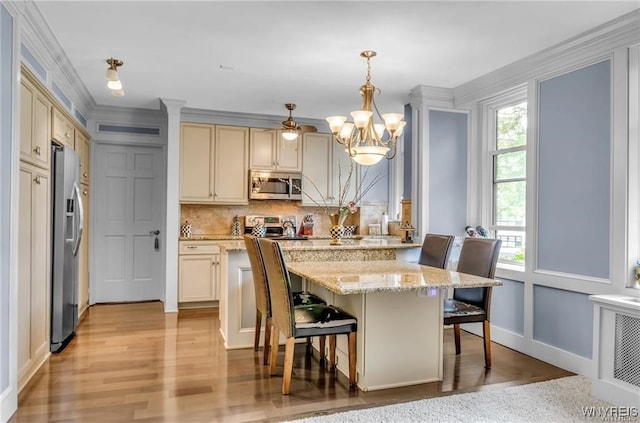 kitchen with cream cabinets, a kitchen bar, decorative light fixtures, light wood-type flooring, and appliances with stainless steel finishes