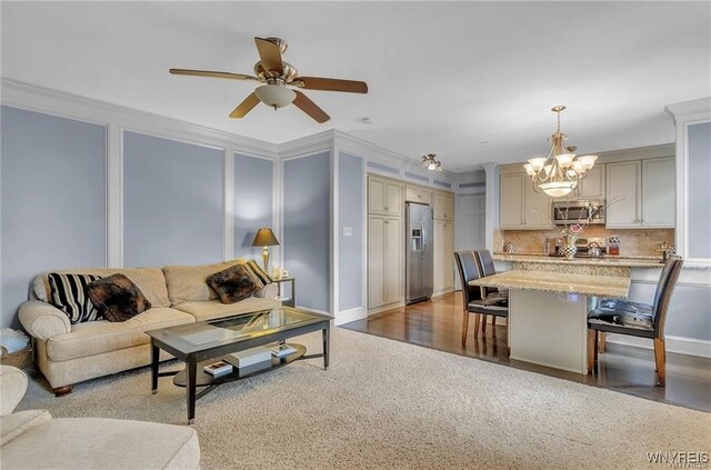 living room featuring ceiling fan with notable chandelier, ornamental molding, and dark hardwood / wood-style floors