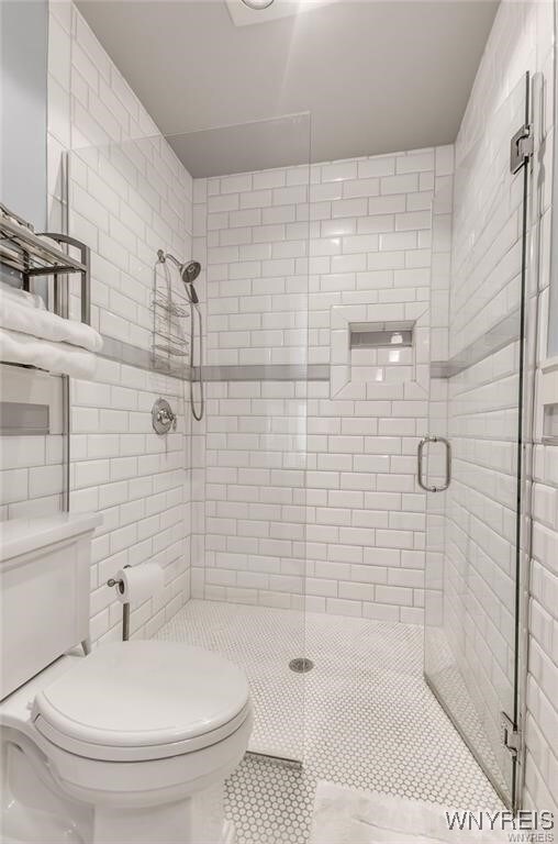 bathroom featuring a shower with door, tile patterned floors, and toilet