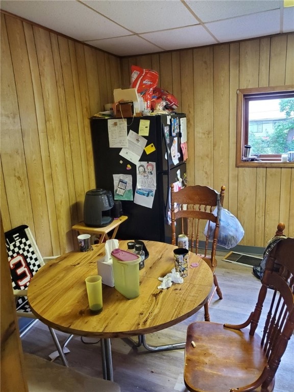 dining space with wood walls, hardwood / wood-style floors, and a paneled ceiling