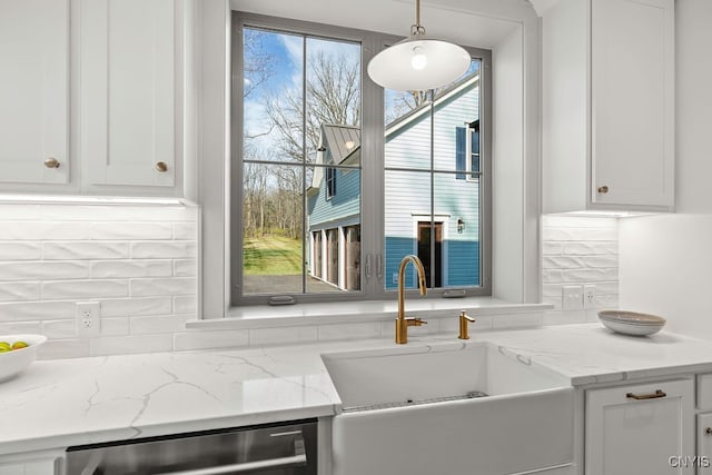 kitchen featuring backsplash, white cabinets, sink, hanging light fixtures, and light stone countertops